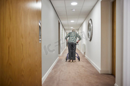 老年妇女的后视图与步行者沿着走廊走在退休之家