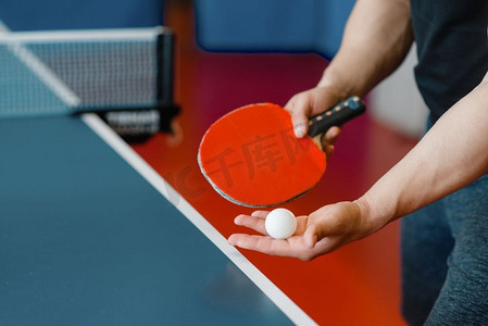 网球摄影照片_男子手拿乒乓球拍和球，在室内锻炼。男子在运动服站在桌子与网，训练在乒乓球俱乐部