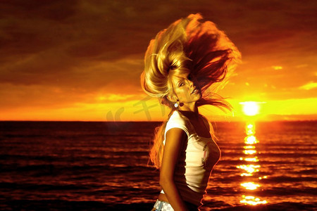 美丽的女孩头发在海上金色的夕阳上飘动。金发运动