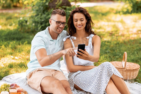 休闲与人的概念快乐夫妇带着智能手机在夏季公园野餐。带着智能手机在公园野餐的幸福情侣
