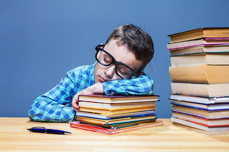 可爱的孩子在学校图书馆的桌子上睡着了。学生戴着眼镜对着许多书。可爱的孩子睡觉在桌子在学校图书馆