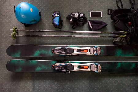 放置在地板上的滑雪配件的俯视图。物品包括头盔、护目镜、滑雪、手套。冬季运动休闲时间概念