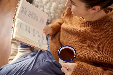 人，季节和休闲概念—年轻妇女在家看书喝咖啡。女人在家里看书喝咖啡