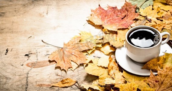 黄色风格摄影照片_秋天的风格。一杯加枫叶的热咖啡。在木制背景上。秋天的风格。一杯加枫叶的热咖啡。