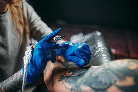 女纹身师用机器在肩膀上纹身。沙龙里的专业纹身。纹身师在男性肩上用机器纹身