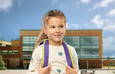 童年和教育理念-背景是背包盖着学校的快乐小女孩。背着书包的快乐小女孩