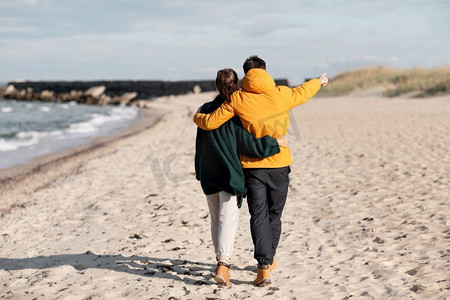 秋天爱情摄影照片_爱情、关系和人的概念-幸福的情侣走在秋天的海滩上。一对情侣沿着秋天的海滩散步