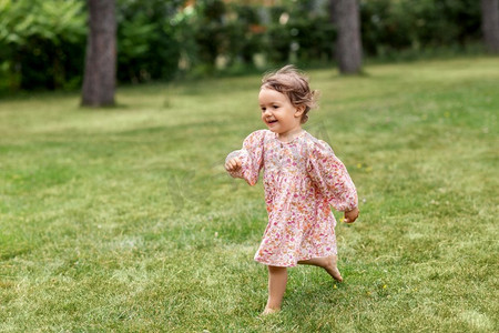 童年、休闲和人的概念快乐的小女婴奔跑在夏日的田野上。快乐的小女婴在夏日田野上奔跑