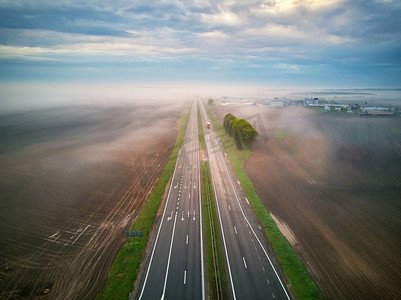 田野路摄影照片_鸟瞰公路被雾覆盖。清晨，薄雾弥漫。路在春天夏天的田野。高速公路在雨天。白俄罗斯、明斯克地区
