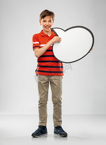沟通和人的概念—微笑的男孩拿着空白的讲话气泡在灰色背景。男孩拿着讲话泡泡