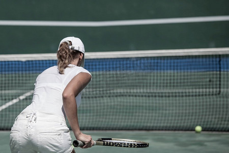 网球摄影照片_身着白色网球服的女子在球场上打网球的背影。一名女子在球场上打网球