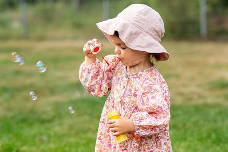 童年，休闲和人的概念—快乐的小女婴吹肥皂泡在夏天。快乐的女婴吹肥皂泡在夏天