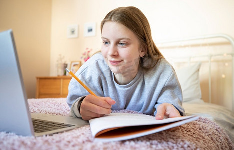 十几岁的女孩躺在卧室的床上，拿着笔记本学习和在家学习