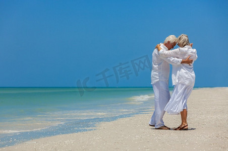 幸福的老年男女退休夫妇在晴朗蓝天的荒凉热带海滩上跳舞度假