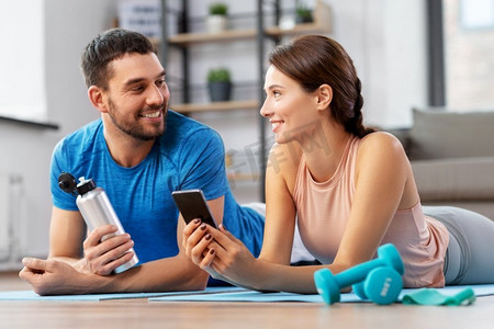 健身情侣摄影照片_健身、运动和科技概念-智能手机在家中休息，这对夫妇很幸福。在家玩完运动后带着智能手机的幸福夫妇