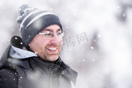 冬日里的男人肖像穿着保暖衣服的年轻人在冬日的森林里享受雪天，雪花环绕着他