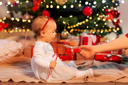 假期和童年概念—母亲在家给小女婴送圣诞礼物。女婴在圣诞树与礼物在家里