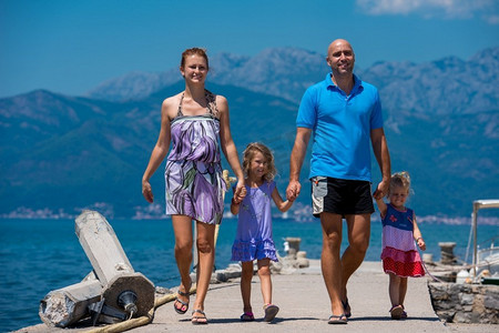 有可爱的小女儿的年轻快乐的家庭拿着他们的手，当走在海边在暑假健康的家庭假日概念