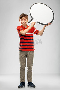 沟通和人的概念—微笑的男孩拿着空白的讲话气泡在灰色背景。男孩拿着讲话泡泡