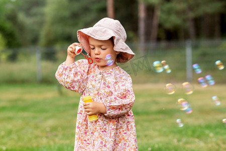 童年，休闲和人的概念—快乐的小女婴吹肥皂泡在夏天。快乐的女婴吹肥皂泡在夏天