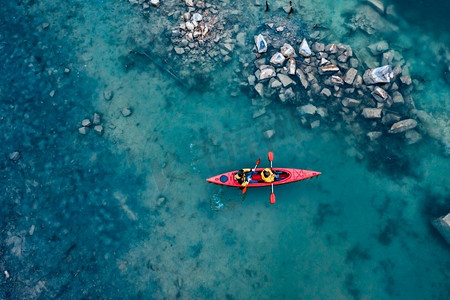 两个运动员漂浮在一艘红色的小船上，平静的蓝色水域。两个运动员漂浮在河中的红船