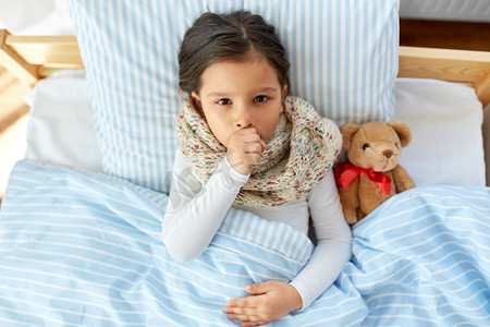 健康，儿童和人的概念—生病咳嗽的女孩躺在床上在家里。生病咳嗽的女孩躺在床上在家里