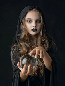 万圣节女巫摄影照片_在万圣节女巫服装和黑暗化妆持有水晶球在白色背景隔绝的小女孩万圣节女巫女孩与水晶球