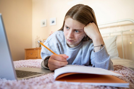 女躺摄影照片_压力女青少年在家庭作业或家庭教育中使用笔记本电脑有问题