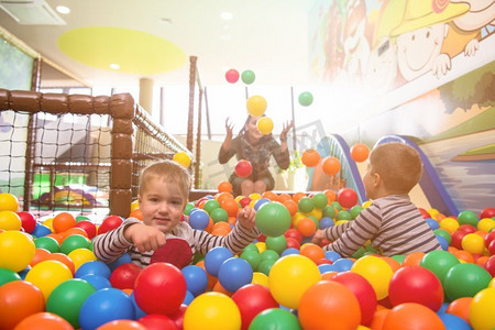 快乐的家庭享受空闲时间年轻妈妈在儿童游戏室与孩子们在游泳池里玩五颜六色的球