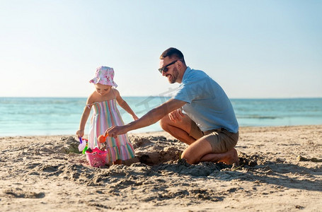 家庭、休闲和人的概念-爸爸和小女儿在夏日海滩玩沙子玩具。父女俩在海滩上玩玩具