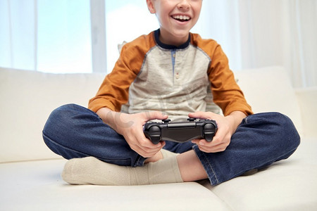 休闲，技术和人的概念—快乐的微笑男孩与游戏手柄玩视频游戏在家里。快乐的男孩与游戏手柄玩视频游戏在家里