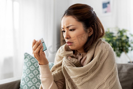 治愈摄影照片_健康，寒冷和人的概念-悲伤的生病的年轻亚洲妇女在家里用毯子和药物。生病的亚裔妇女在家服药