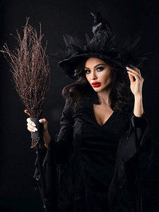 有扫帚的迷人的万圣节女巫在黑色背景，妇女美丽肖像，艺术化妆和服装。迷人的万圣节女巫与扫帚