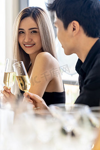 年轻的亚洲成人夫妇庆祝新年圣诞假期与起泡葡萄酒一起在大公寓的客厅在大城市