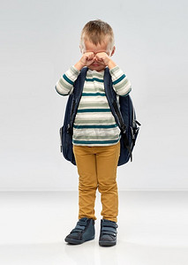 学前教育和童年概念—哭泣的小男孩有学校背包在灰色背景。哭泣的小男孩背着书包