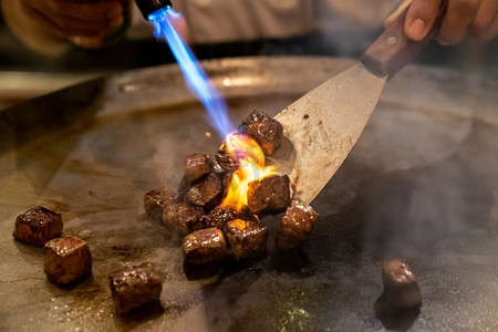 骰子摄影照片_铁板烧牛肉食谱日本烤牛肉在带刮刀和煤气灶的平底锅上烹调