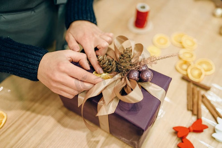 圣诞节手摄影照片_女性用冷杉球果、手工包装和装饰工艺装饰圣诞礼盒。餐桌上的女式包裹，装饰程序