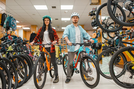 戴着自行车头盔的情侣选择自行车，在体育商店购物。夏季极致生活方式，活跃的休闲商店，顾客购买周期