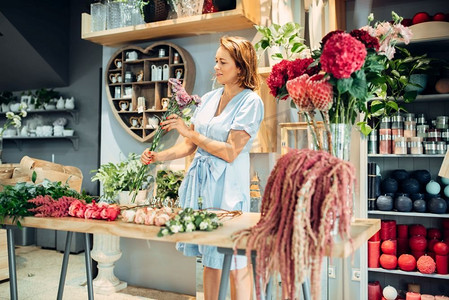 女花艺师在商店的桌子上挑选鲜花。  花店制作花束在工作场所在精品店