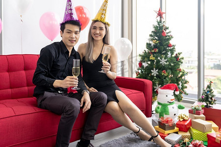大城市摄影照片_年轻的亚洲成人夫妇庆祝新年圣诞假期与起泡葡萄酒一起在大公寓的客厅在大城市