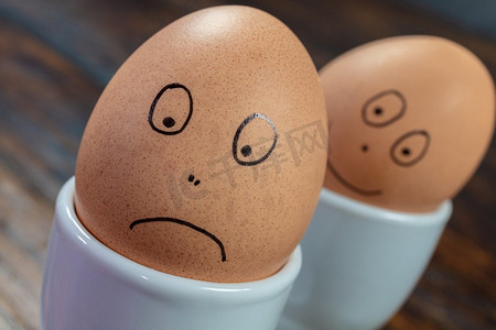 情感概念两个煮鸡蛋在白色蛋杯与绘制的快乐和悲伤的脸在一张木桌