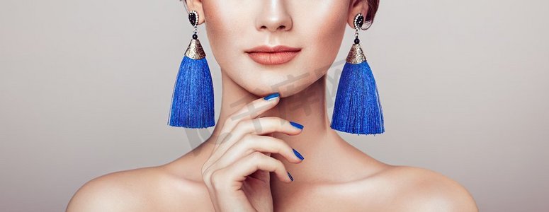 美丽的女人与大耳环流苏珠宝蓝色颜色。完美的化妆和指甲美甲
