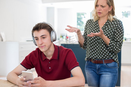 十几岁的男孩戴着耳机和使用手机被母亲唠叨在家里