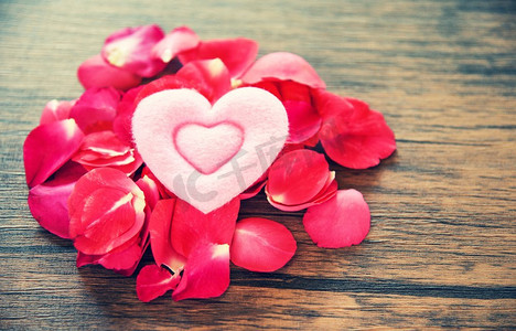 玫瑰创意设计摄影照片_情人节爱的心浪漫的概念/堆玫瑰花瓣与粉红色的心装饰在木桌质朴的背景 