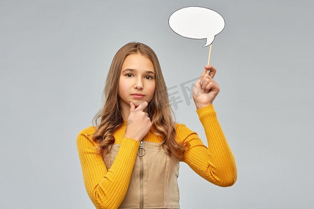 沟通和人的概念—微笑的少女拿着空白的讲话气泡在灰色背景。十几岁的女孩拿着讲话泡沫