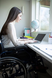 十几岁的女孩在轮椅上学习在家里的笔记本电脑