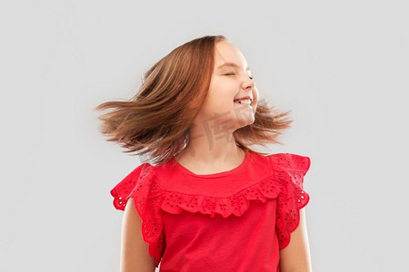 飘动摄影照片_童年与人的概念-美丽的微笑女孩穿着红色衬衫，灰色背景下挥舞着头发。穿着红色衬衫，头发飘动的快乐女孩