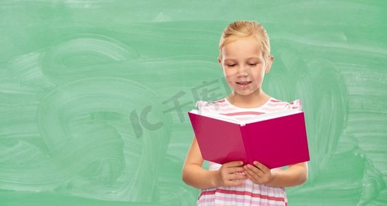 童年和人概念—微笑的小女孩读书在绿色黑板背景的书微笑的小女孩读书在学校