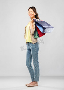 销售，出口和消费主义概念—有购物袋的愉快的亚洲年轻妇女在灰色背景快乐的亚洲女人与购物袋