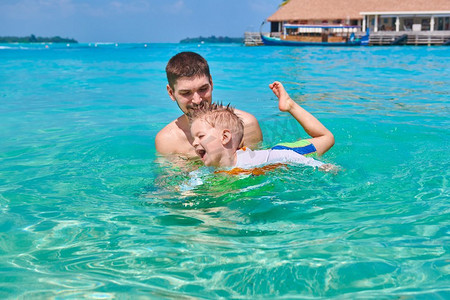 暑假游泳摄影照片_三岁的学步男孩和父亲一起学习游泳。暑假全家去马尔代夫度假。